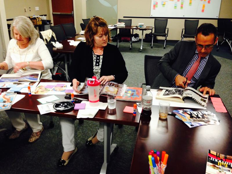 Faculty and staff around a long table, cutting and arranging images for a collage exercise.