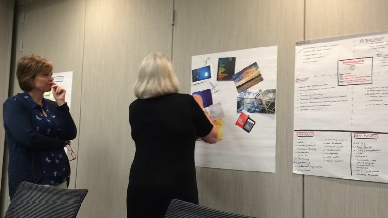 Two people in conversation beside a wall of posters and notes.