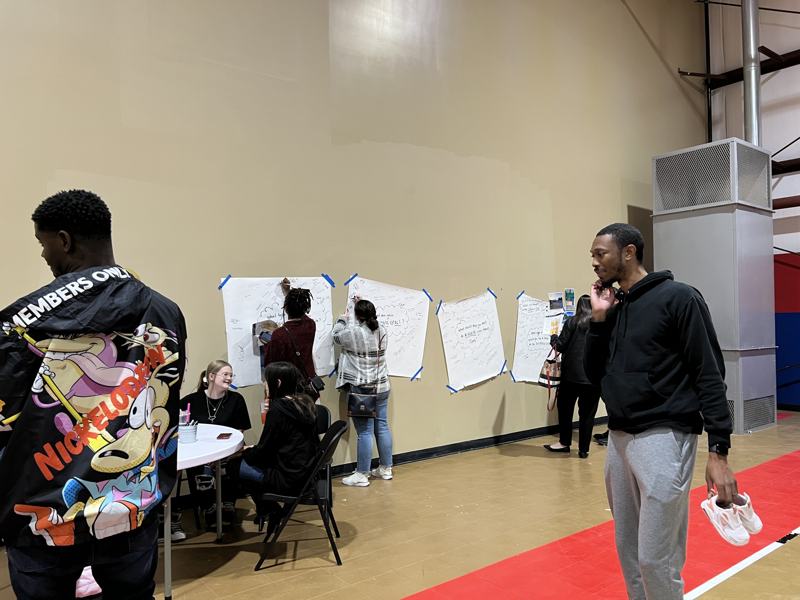 Residents writing on posters along a wall while others sit at a nearby table.