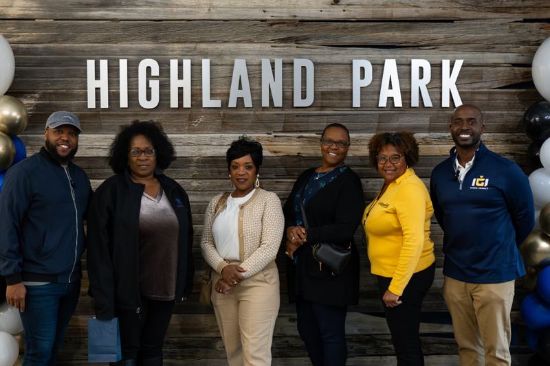 A group of seven people standing together in front of a Highland Park sign.